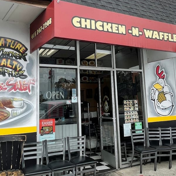 Keith's Chicken N Waffles storefront with a red awning, murals, and chairs outside.