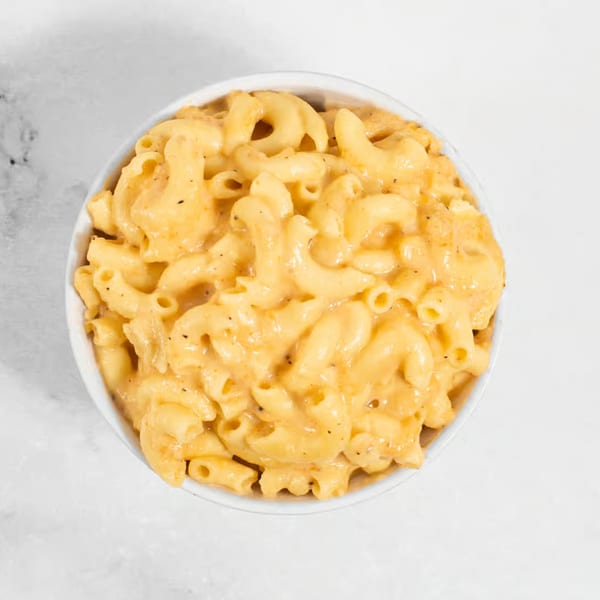 A white bowl filled with creamy macaroni and cheese, topped with black pepper, on a white surface.
