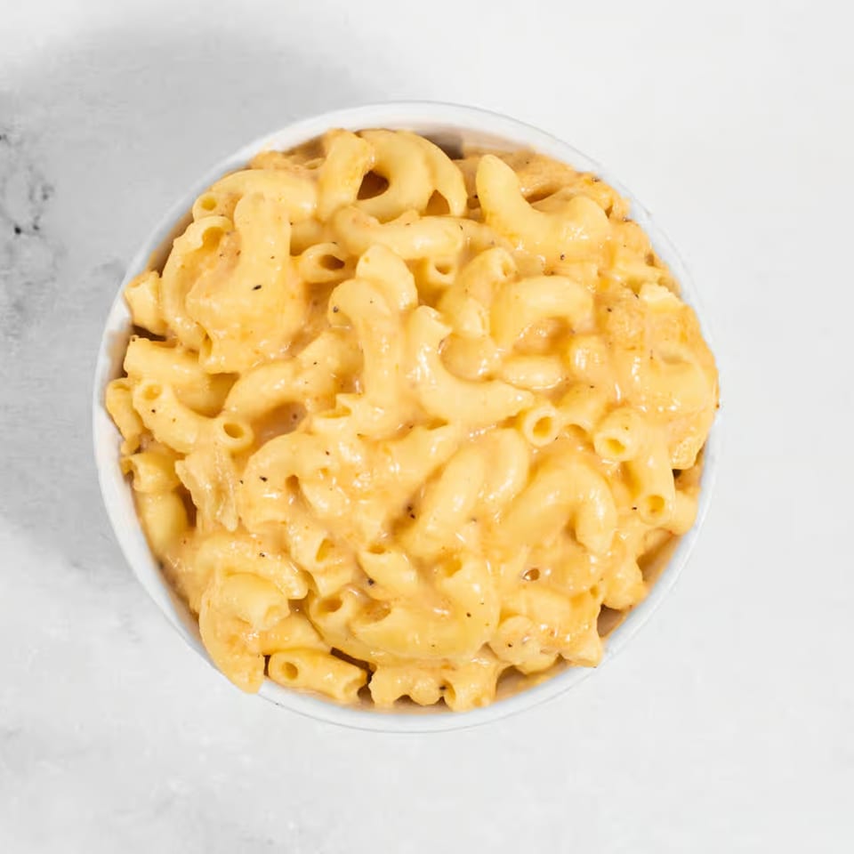 A white bowl filled with creamy macaroni and cheese, topped with black pepper, on a white surface.