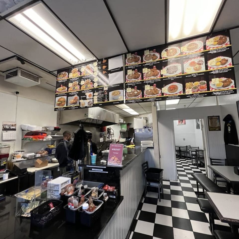 Interior of Keith’s Chicken N Waffles, showing menu boards, a counter, and a dining area with checkered floors.