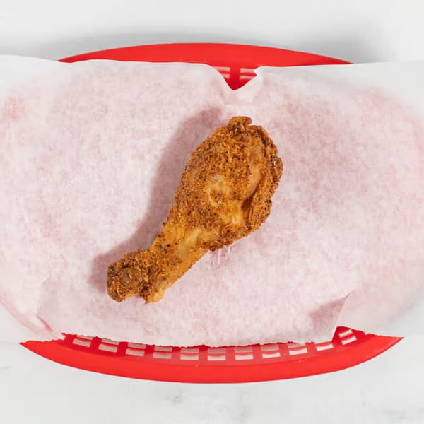 Crispy fried chicken drumstick in a red basket lined with white paper, from Keith's Chicken N Waffles.
