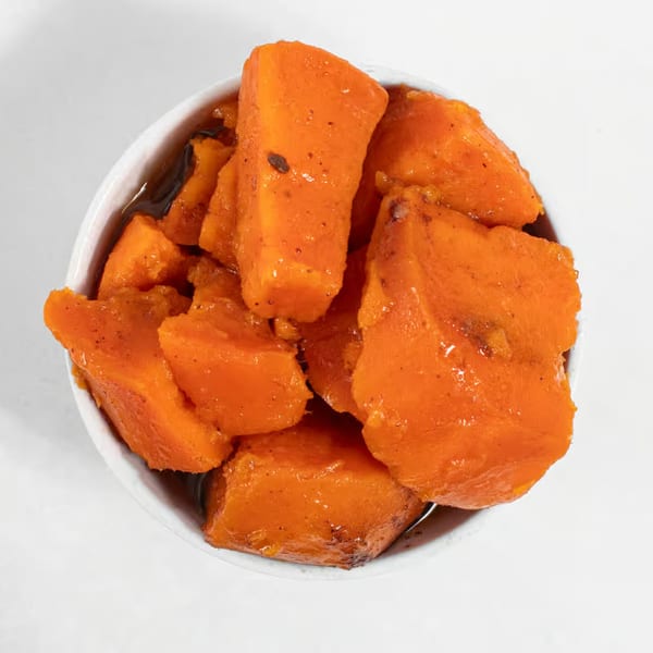 Close-up overhead view of candied yams in a white bowl, glistening with syrup.