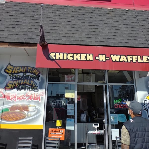 Exterior of Keith's Chicken N Waffles, with a mural of chicken and waffles, and a person entering.